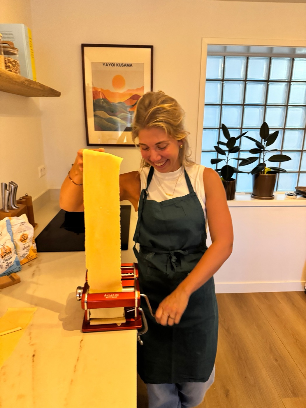 Carmen rolt lachend een vel pastadeeg uit met een pastamachine
